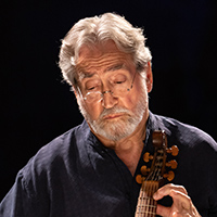 Jordi Savall, an older Spanish man with gray hair, sits looking down at a music stand while playing the viol.