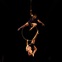 Photo of two members of Cirque Kalabanté in aerialist act, one sitting on top of the circle and one hanging at the bottom
